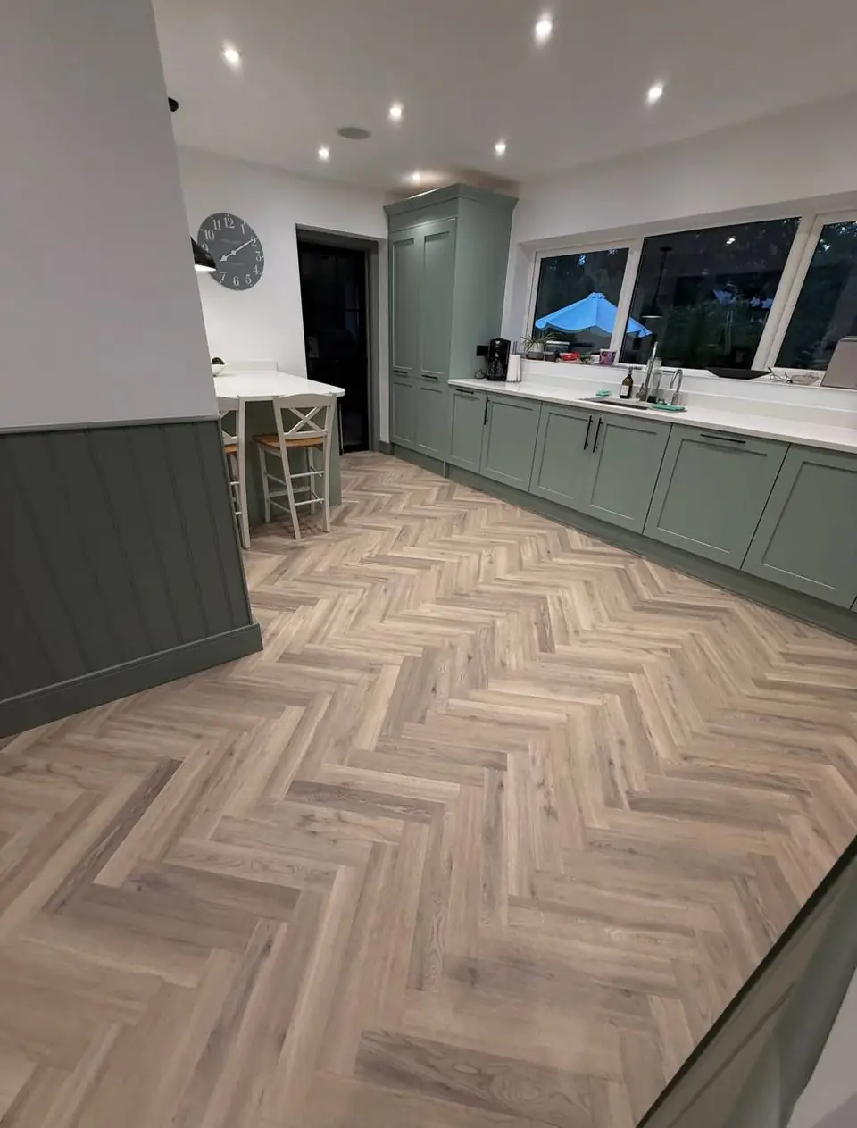 Herringbone floor running into a green kitchen with panelled walls