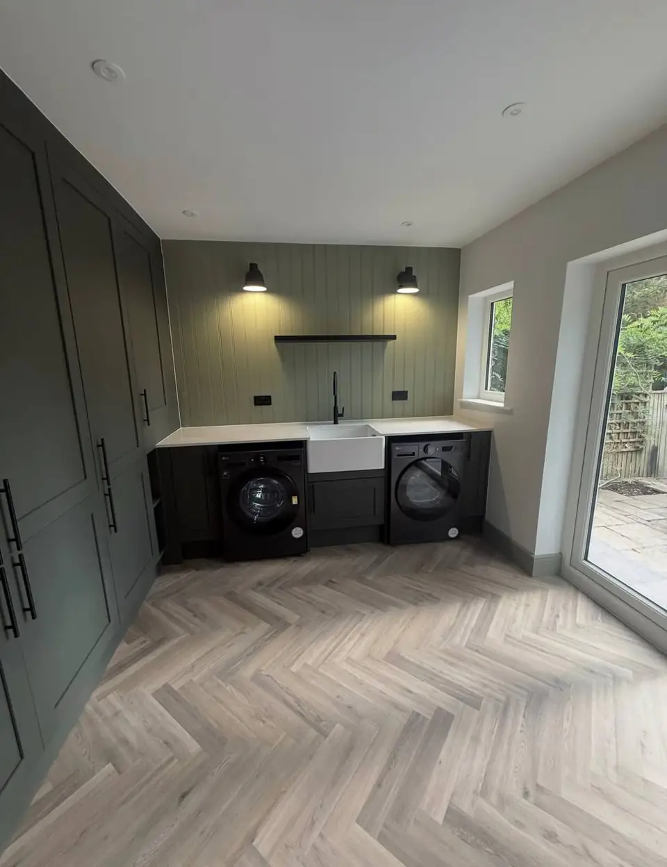 Utility room with tall green cabinets, a Belfast sink, a washing machine, a dryer and panelled walls