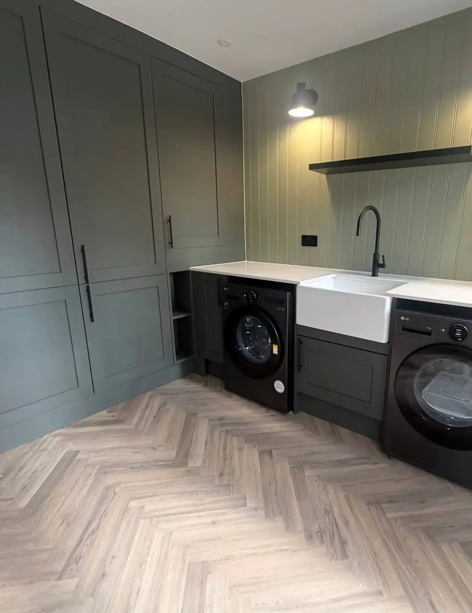 Green utility cupboards beside a Belfast sink, washing machine and dryer on a herringbone floor
