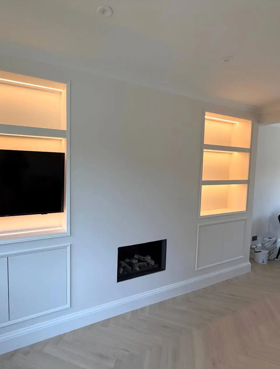 Alcove shelves lit with LED strips either side of a fireplace, TV in one alcove