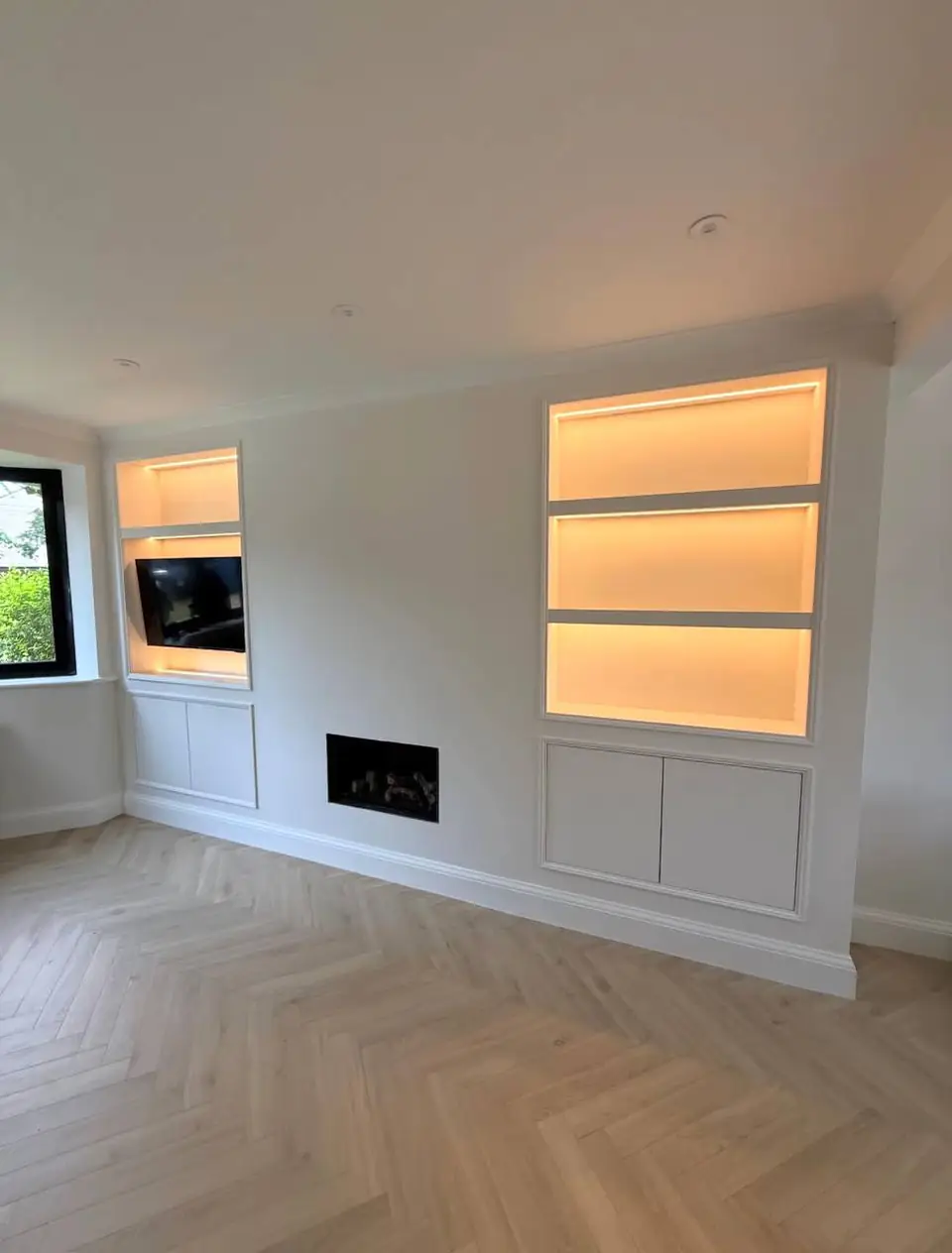 Built-in alcove shelving with warm LED lighting and cupboards below, herringbone floor
