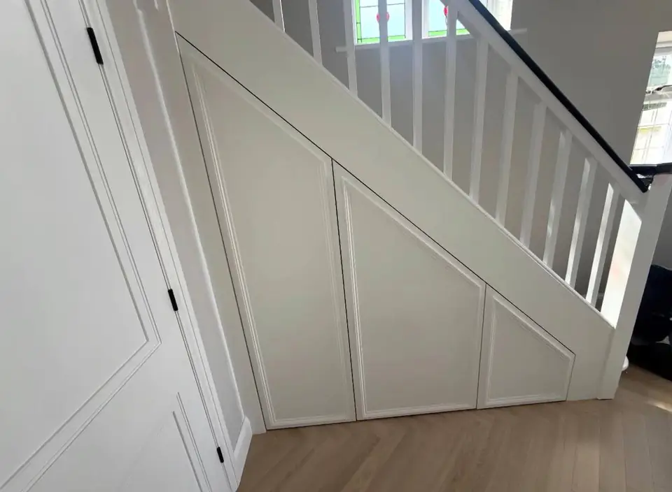 Painted under-stairs cupboards following the line of a white staircase