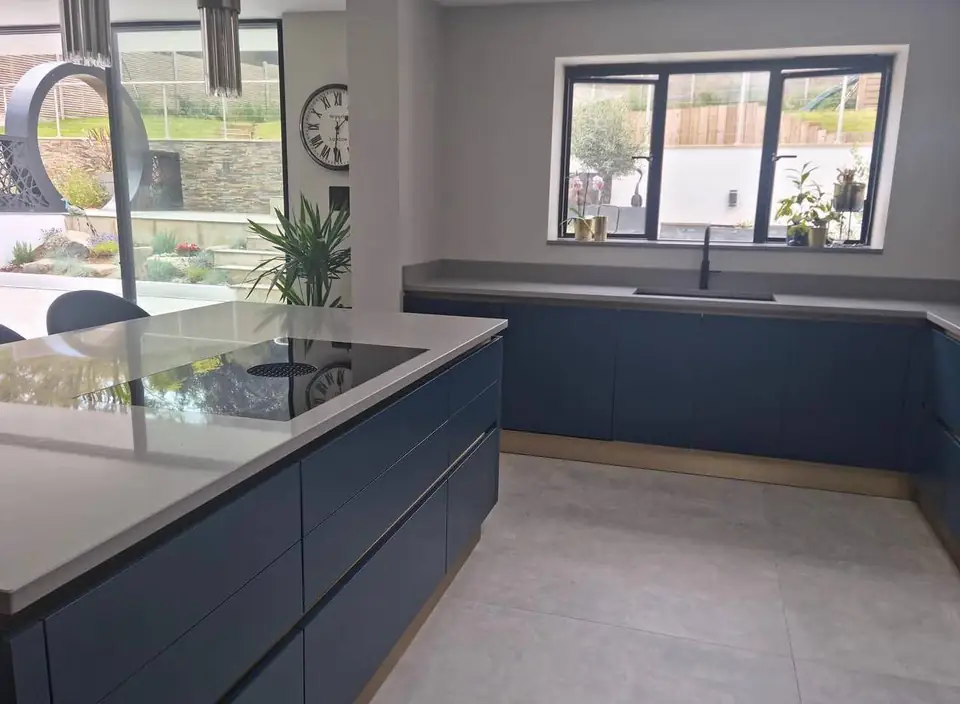 Run of handleless navy units with a grey worktop under a wide window, island hob in front