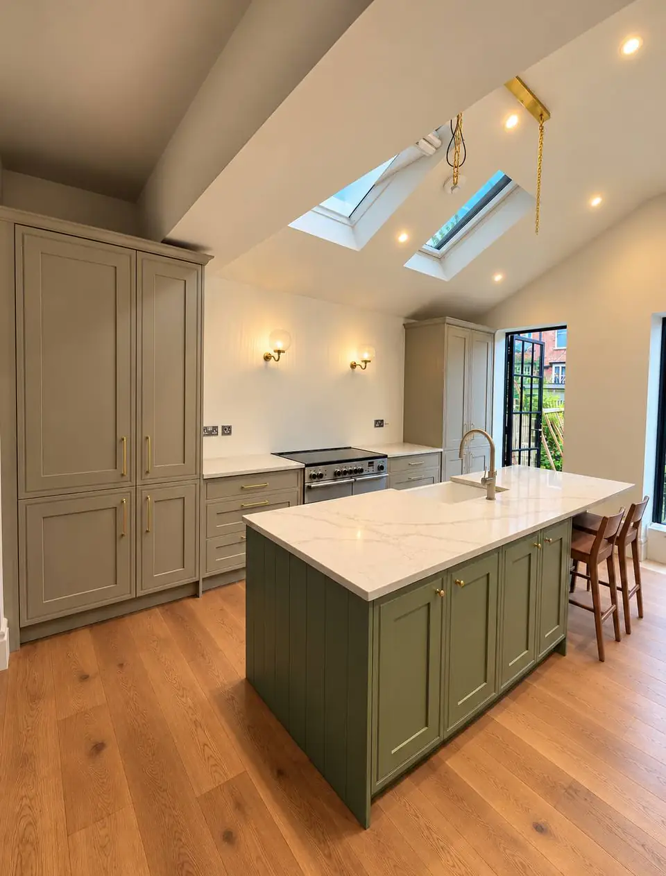 Sage green Shaker kitchen with an island, a marble-effect worktop and an oak floor under roof windows