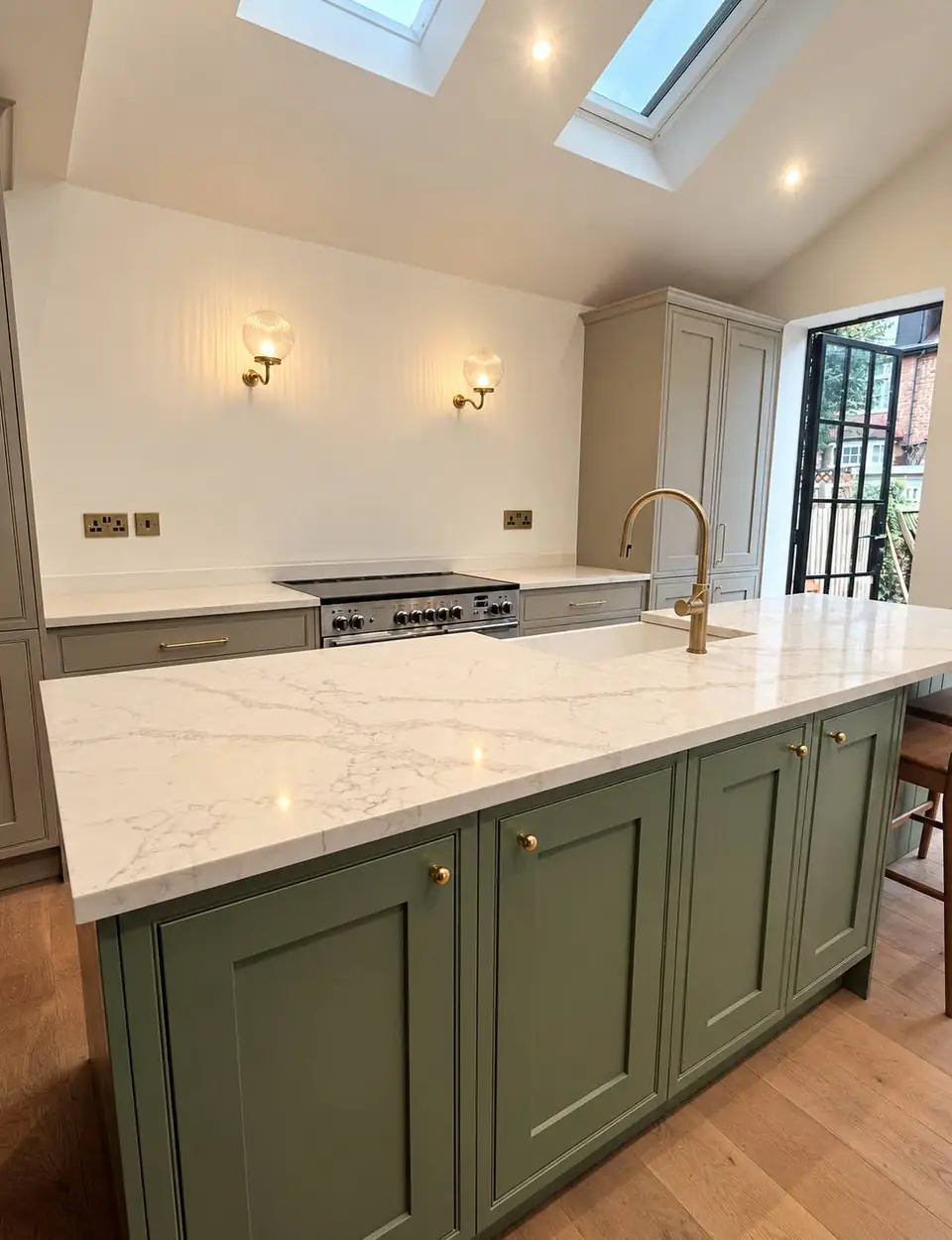 Sage green island with a marble-effect worktop and brass handles, range cooker behind