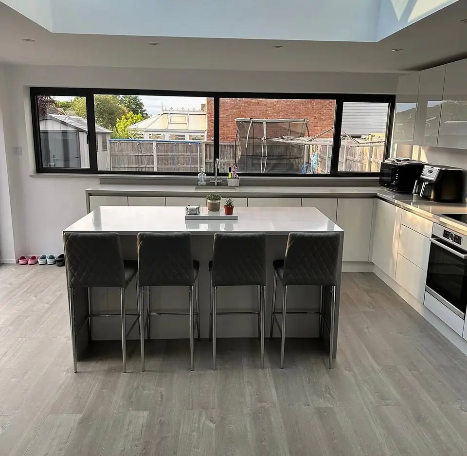 White gloss kitchen with an island and four grey bar stools under a roof lantern