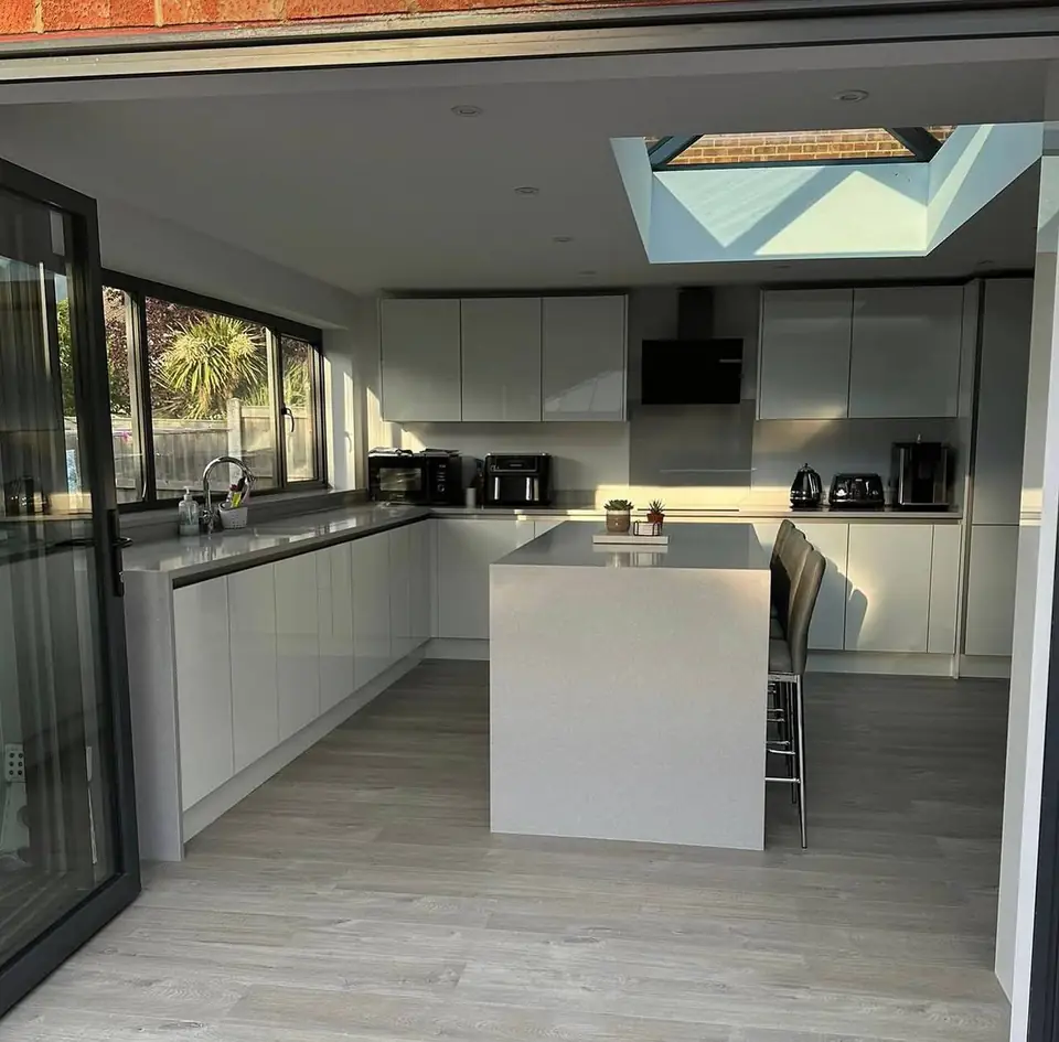 White gloss kitchen with an island seen through open folding doors, roof lantern above