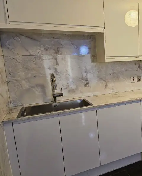 White gloss kitchen units with a steel sink and a marble-effect splashback