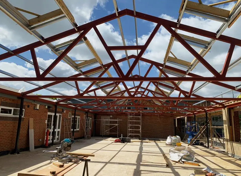 Steel roof trusses in red primer under a glazed roof, London project