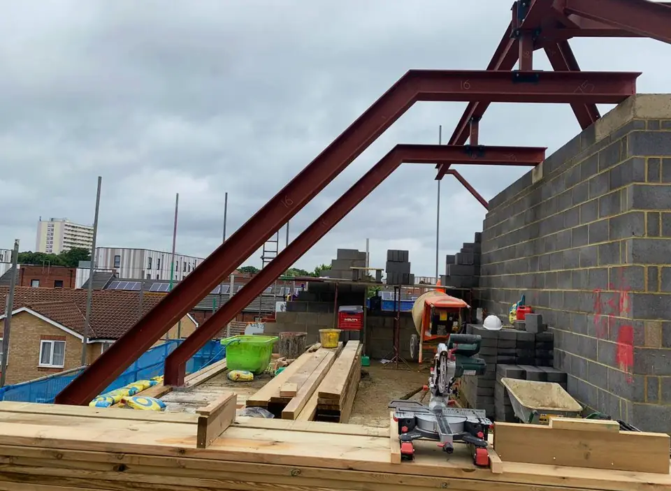 Red steel portal frame above blockwork walls, London project